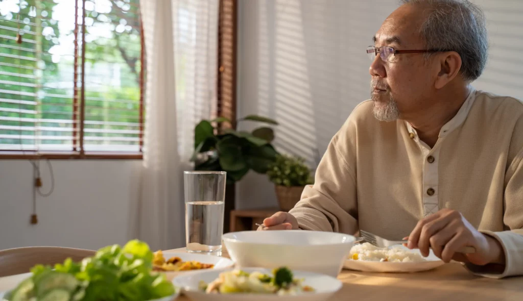 Senhor de idade asiático olha para janela enquanto se alimenta com uma refeição saudável