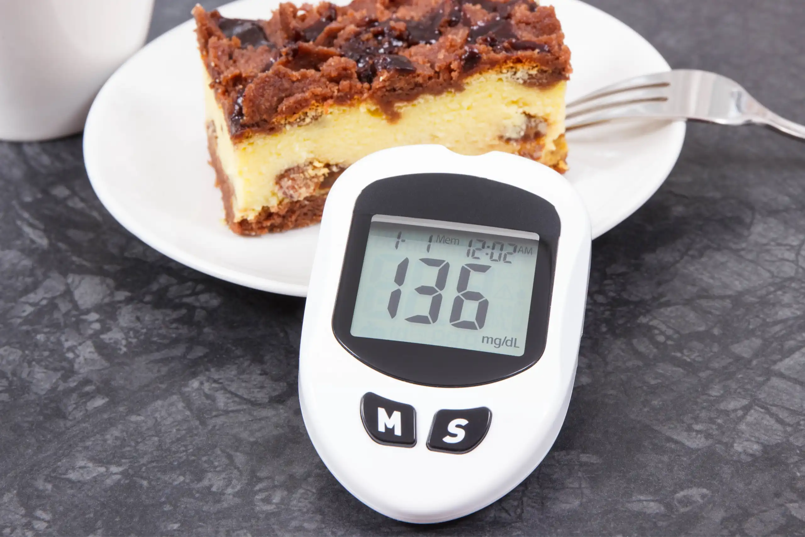 aparelho medidor de glicose apoiado em um prato com um doce enquanto afere um resultado.